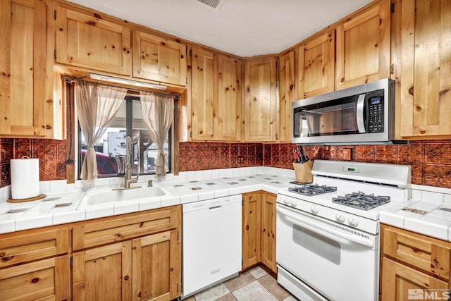 kitchen with a sink, light countertops, tasteful backsplash, and white appliances