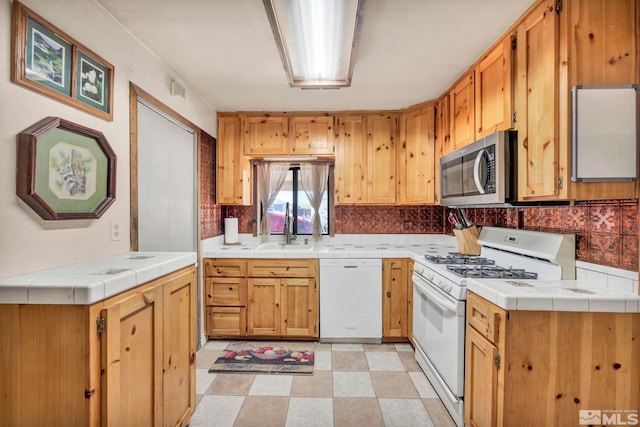 kitchen with a sink, white appliances, tile counters, decorative backsplash, and light floors