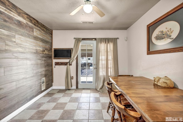 entryway featuring wooden walls, a textured ceiling, a ceiling fan, baseboards, and visible vents