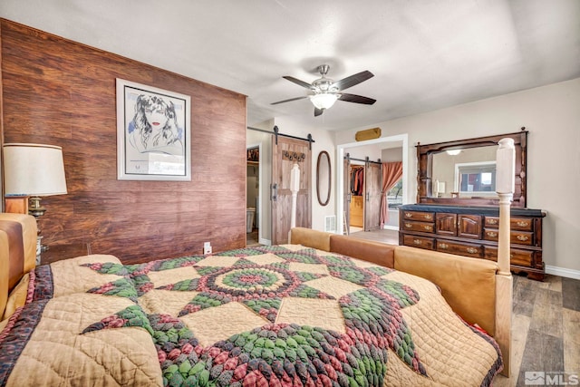 bedroom with a walk in closet, a ceiling fan, a barn door, wood finished floors, and baseboards
