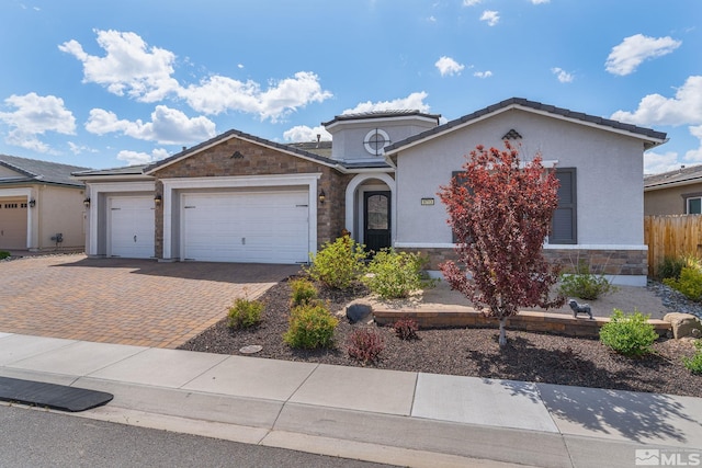 view of front facade featuring fence, an attached garage, stone siding, stucco siding, and decorative driveway