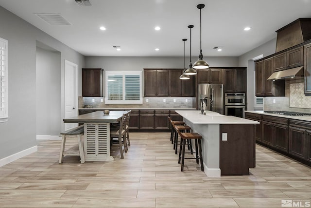 kitchen featuring visible vents, a kitchen island with sink, under cabinet range hood, appliances with stainless steel finishes, and backsplash