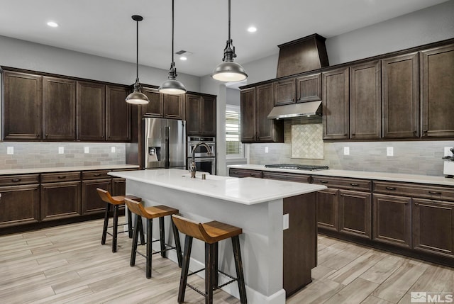 kitchen with appliances with stainless steel finishes, light countertops, tasteful backsplash, under cabinet range hood, and a kitchen bar