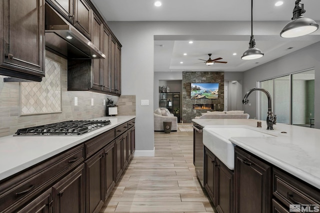 kitchen featuring a ceiling fan, tasteful backsplash, a fireplace, a sink, and stainless steel appliances