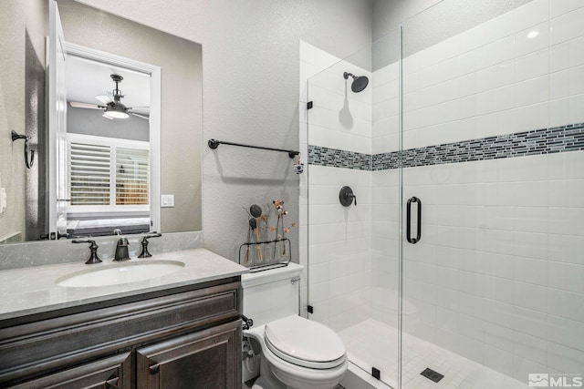 bathroom featuring ceiling fan, a stall shower, vanity, toilet, and a textured wall