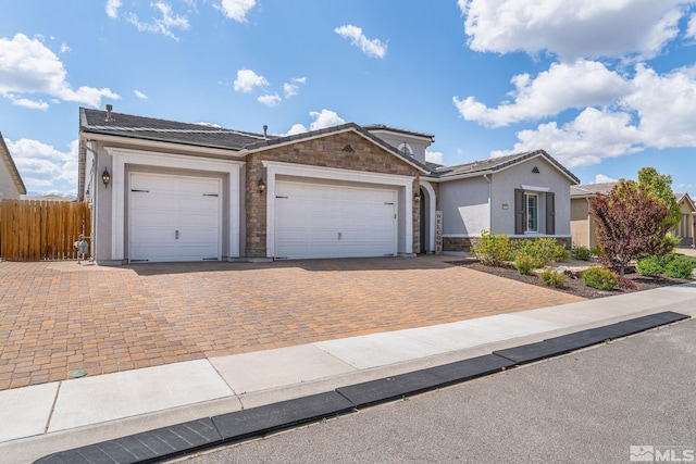 ranch-style home with fence, stone siding, decorative driveway, stucco siding, and an attached garage