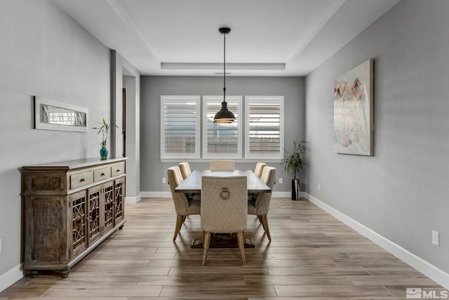dining area with a raised ceiling, baseboards, and light wood finished floors