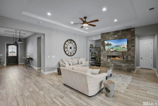 living area featuring visible vents, a ceiling fan, a raised ceiling, and a fireplace