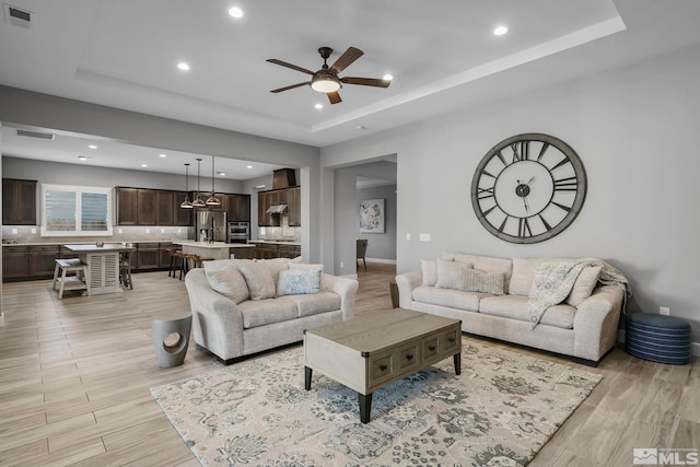 living area with ceiling fan, a tray ceiling, recessed lighting, and visible vents