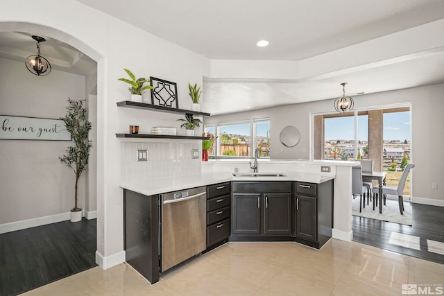 kitchen with stainless steel dishwasher, baseboards, light countertops, arched walkways, and a sink