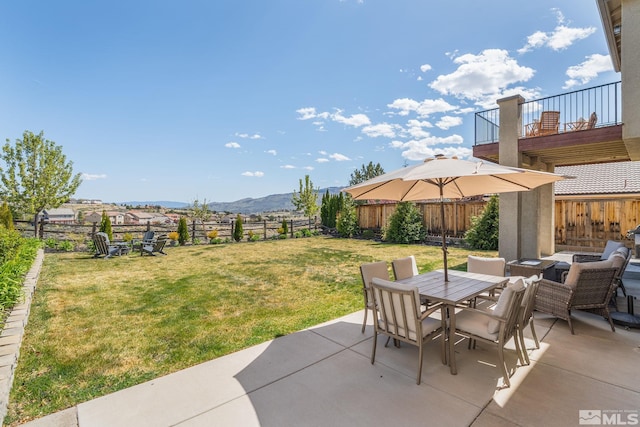 view of patio with a mountain view, outdoor dining area, a fenced backyard, and a balcony