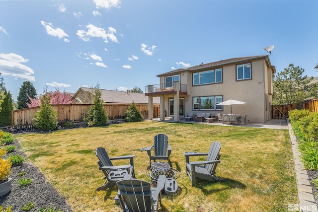 back of house featuring a balcony, a patio, a fenced backyard, stucco siding, and a yard
