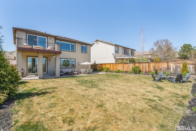 rear view of house featuring a balcony, a fenced backyard, a patio, a fire pit, and stucco siding