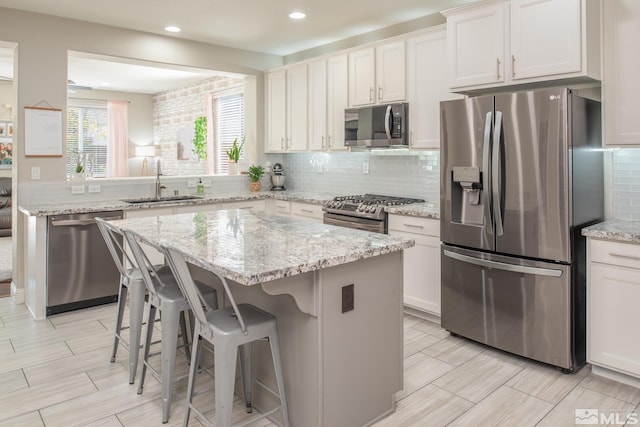 kitchen featuring appliances with stainless steel finishes, a sink, a kitchen breakfast bar, a center island, and tasteful backsplash