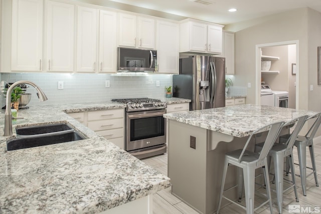 kitchen featuring decorative backsplash, washing machine and dryer, a breakfast bar, a sink, and stainless steel appliances