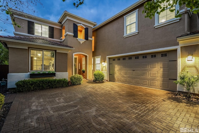 traditional home featuring decorative driveway, a garage, and stucco siding