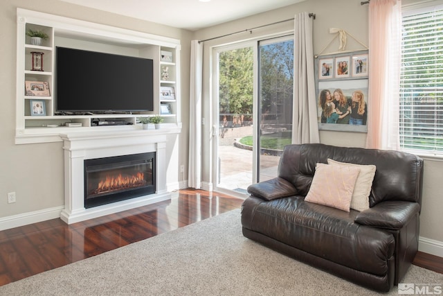 living area with baseboards, a glass covered fireplace, and wood finished floors