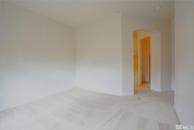 spare room with light colored carpet, arched walkways, and baseboards
