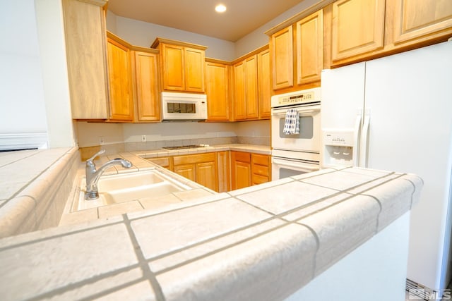kitchen featuring light brown cabinetry, a sink, a peninsula, tile counters, and white appliances