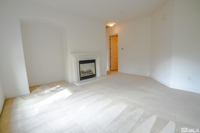 unfurnished living room with a fireplace with raised hearth and light colored carpet