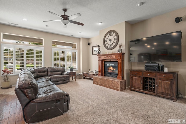 living area with a ceiling fan, a textured ceiling, visible vents, hardwood / wood-style flooring, and a glass covered fireplace