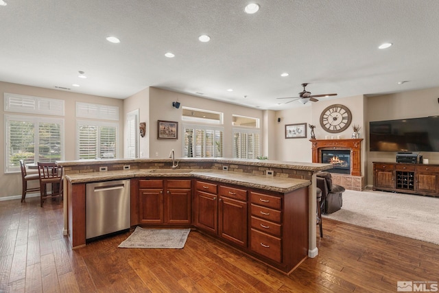 kitchen with stainless steel dishwasher, a tile fireplace, a sink, dark wood-style floors, and open floor plan
