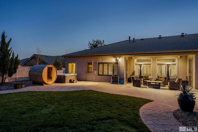 back of house featuring an outdoor living space, a lawn, a patio area, a hot tub, and stucco siding