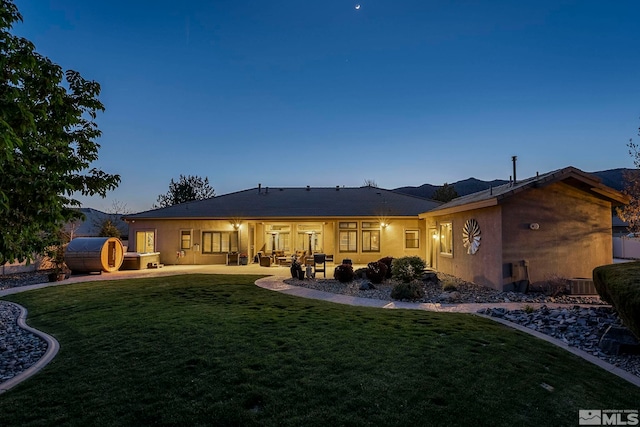 back of property at dusk featuring a patio area, central air condition unit, and a yard