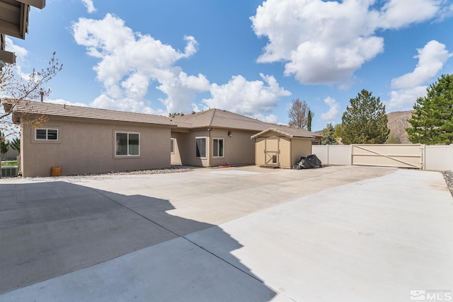 rear view of house featuring an outdoor structure, fence, a patio, a storage unit, and a gate