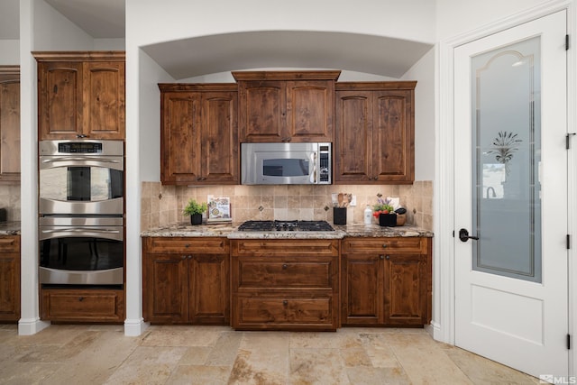 kitchen featuring appliances with stainless steel finishes, light stone countertops, backsplash, and lofted ceiling