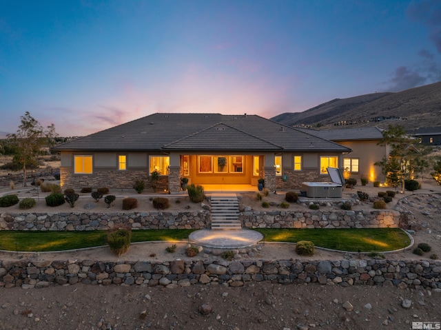 rear view of house featuring stone siding, cooling unit, a lawn, a hot tub, and a mountain view