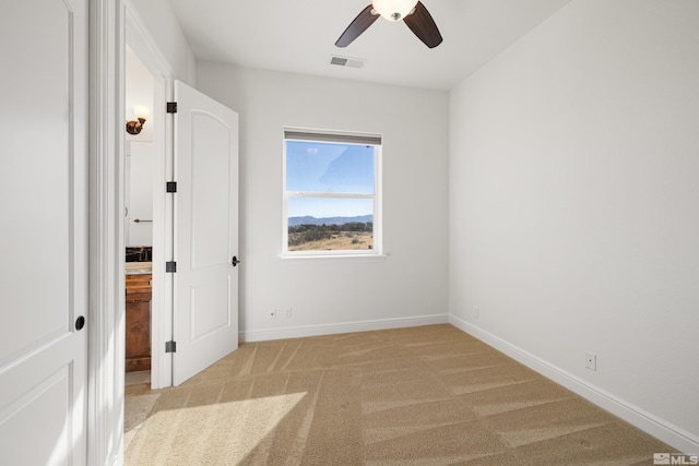 unfurnished bedroom with ceiling fan, visible vents, light colored carpet, baseboards, and ensuite bath