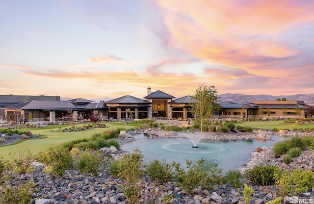 back of house at dusk with a water view, a standing seam roof, a chimney, and metal roof