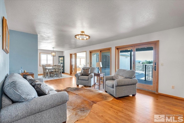 living room with a textured ceiling, baseboards, and light wood-style flooring