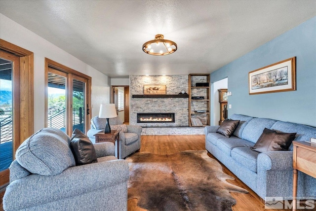 living room with a stone fireplace, wood finished floors, and a notable chandelier