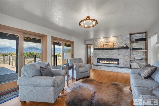 living room featuring a textured ceiling, a notable chandelier, a stone fireplace, and wood finished floors