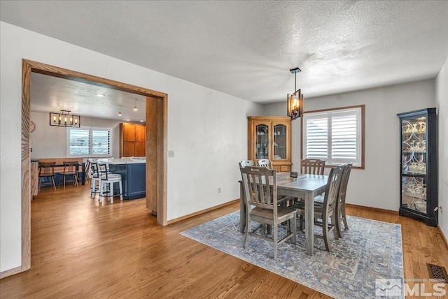 dining room with a textured ceiling, a chandelier, wood finished floors, and visible vents
