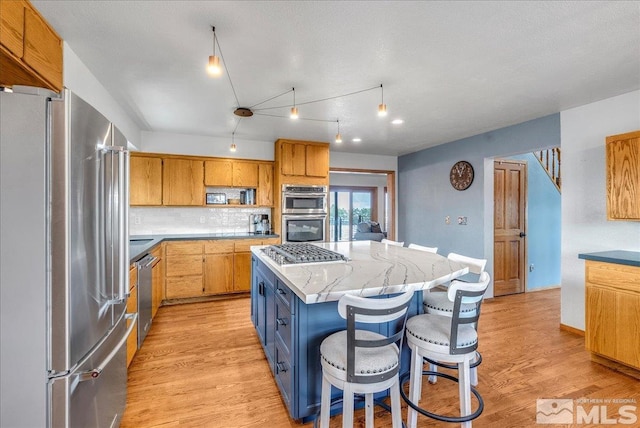 kitchen with light stone countertops, appliances with stainless steel finishes, decorative backsplash, light wood-type flooring, and a kitchen island
