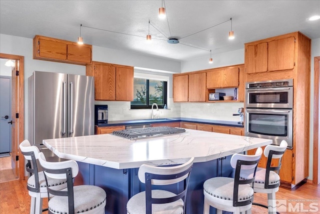 kitchen with a kitchen island, light wood-type flooring, a sink, backsplash, and stainless steel appliances