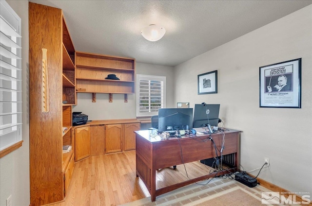 home office with light wood-type flooring and a textured ceiling