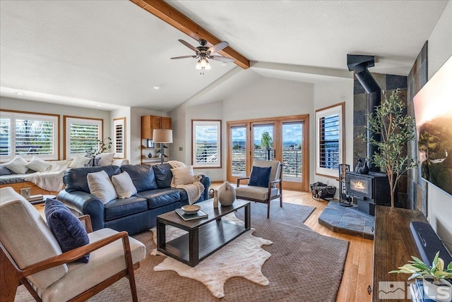 living room with a ceiling fan, lofted ceiling with beams, a wood stove, and light wood-type flooring