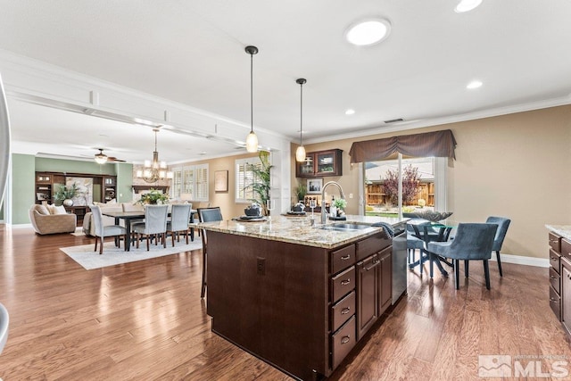 kitchen with dark brown cabinets, hanging light fixtures, a sink, dishwasher, and wood finished floors