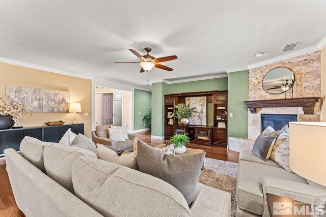 living room featuring a ceiling fan, visible vents, crown molding, a tiled fireplace, and wood finished floors