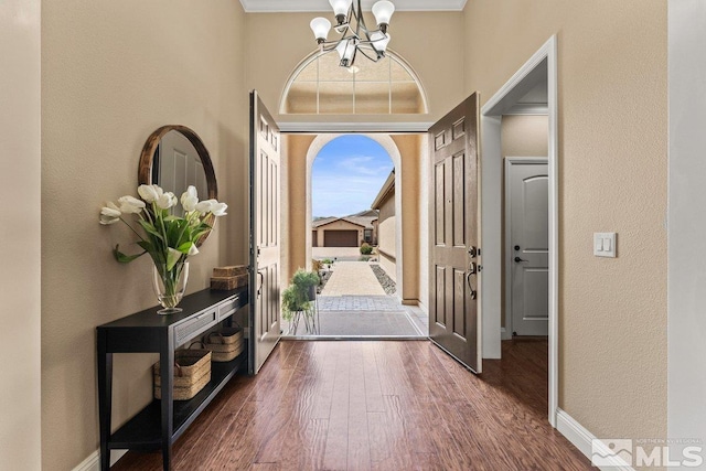 entryway with a towering ceiling, wood finished floors, baseboards, a chandelier, and a textured wall