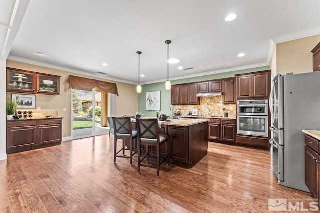 kitchen featuring a breakfast bar area, appliances with stainless steel finishes, tasteful backsplash, a center island, and wood finished floors
