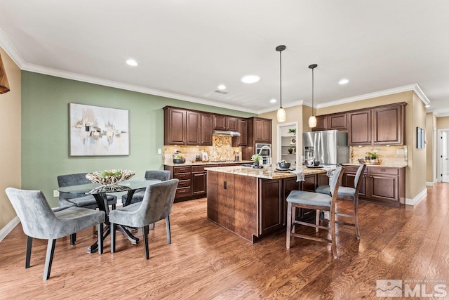 kitchen with a kitchen island with sink, tasteful backsplash, dark wood-style floors, a breakfast bar, and under cabinet range hood