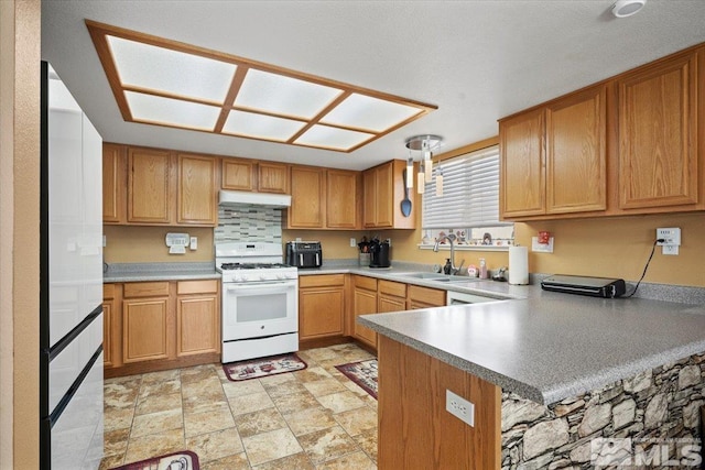 kitchen featuring a sink, light countertops, a peninsula, white range with gas stovetop, and under cabinet range hood