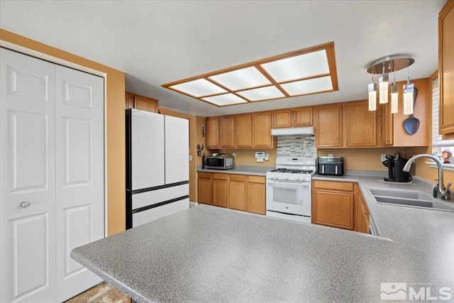 kitchen featuring a peninsula, white appliances, light countertops, under cabinet range hood, and a sink