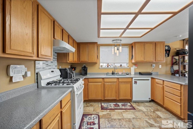 kitchen with white appliances, light countertops, under cabinet range hood, a sink, and stone finish flooring