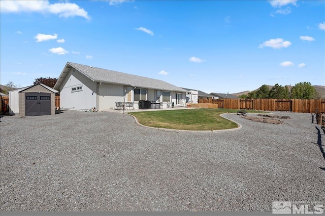 back of property with an outdoor structure, a shed, a fenced backyard, a yard, and a patio